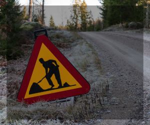 Grusväg i gles skog. i förgrunden vägarbetwsskylt som är symbolisk för texten
